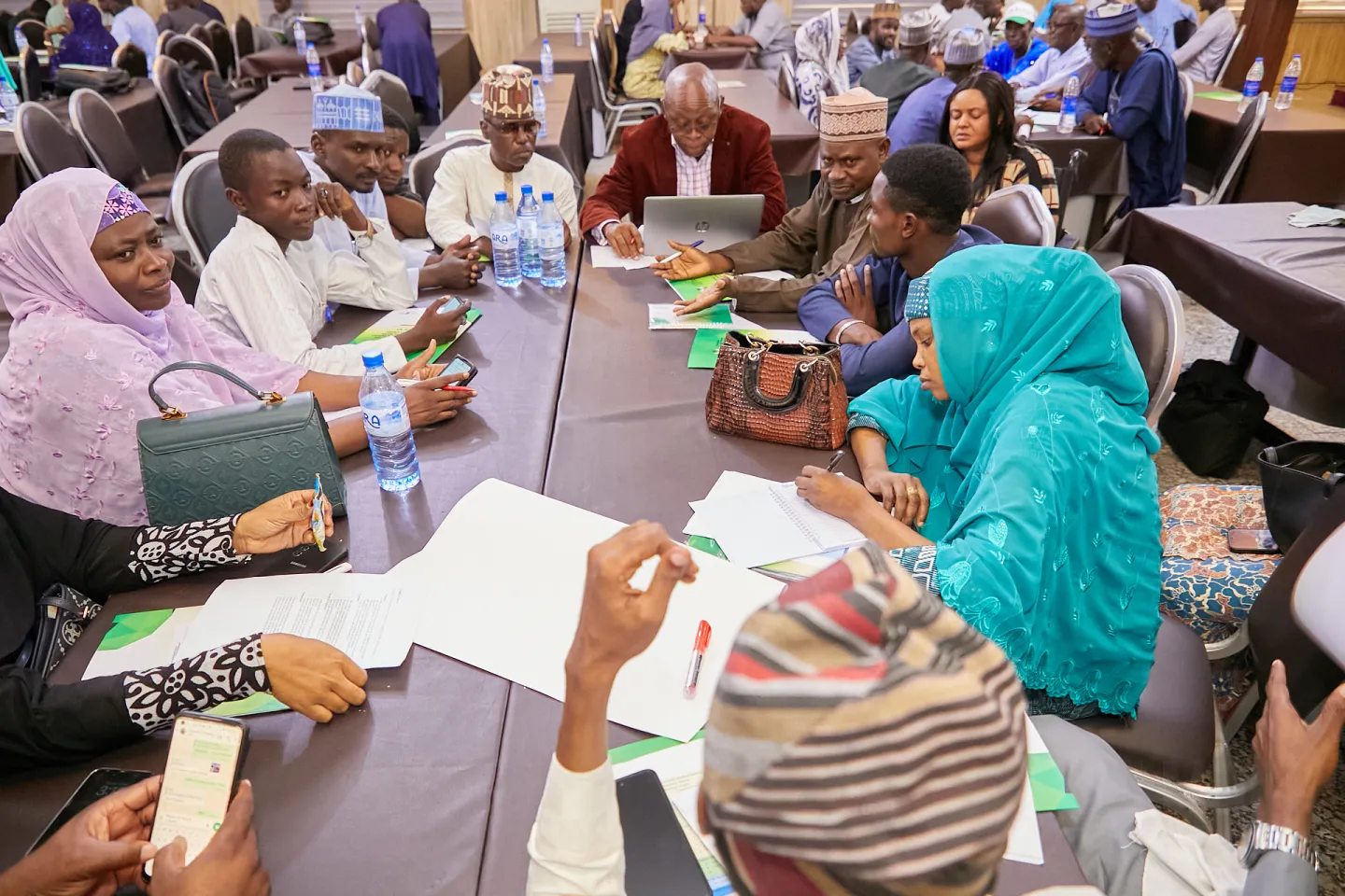 Participants are engaged in collaborative discussions around tables, with documents and materials in use.