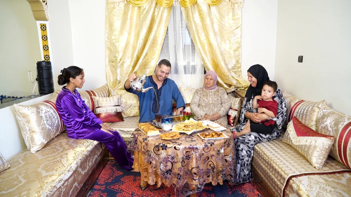 Fatima Laanieg sits in a living room with her family including her mother, a teenage daughter and her toddler nephew. Her husband pours tea.