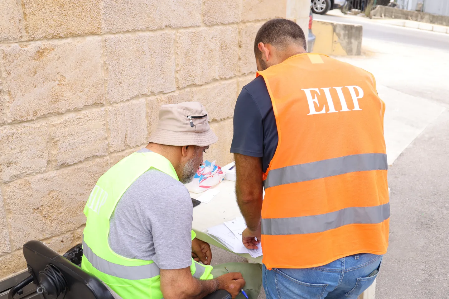 Raymond Khoury seated on his wheelchair and working with an ILO EIIP team member