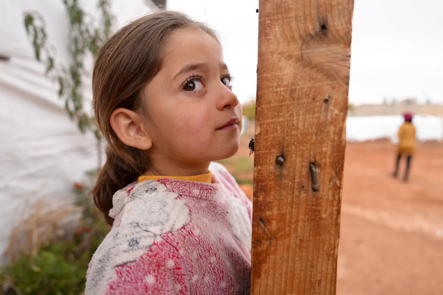 Young Syrian girl Amena stands outside the tent where she lives with her family in the Bekaa Valley, a few metres from the fields where they work, 15 December 2025. 