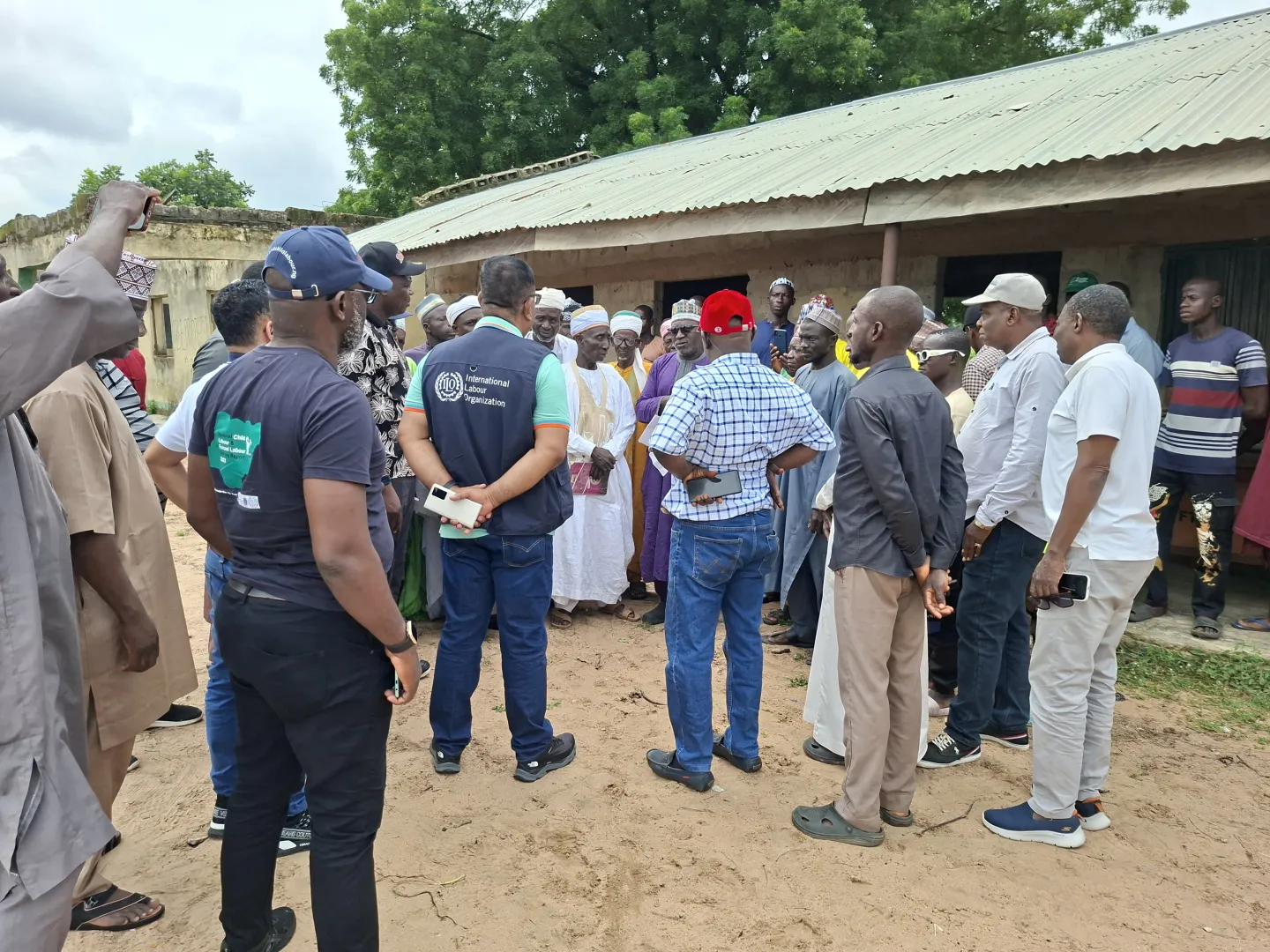 ILO technical team and community leaders gather outside a rural building in Niger State to discuss strategies for sustainable road maintenance under the RAAMP project, emphasizing local ownership and job creation.