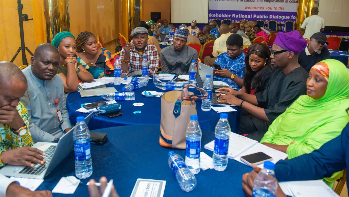 Participants seated around a table during a breakout session at the National Dialogue on Skills Development in Abuja. The table is covered with documents, laptops, and bottled water, indicating active discussions and collaborative work.
