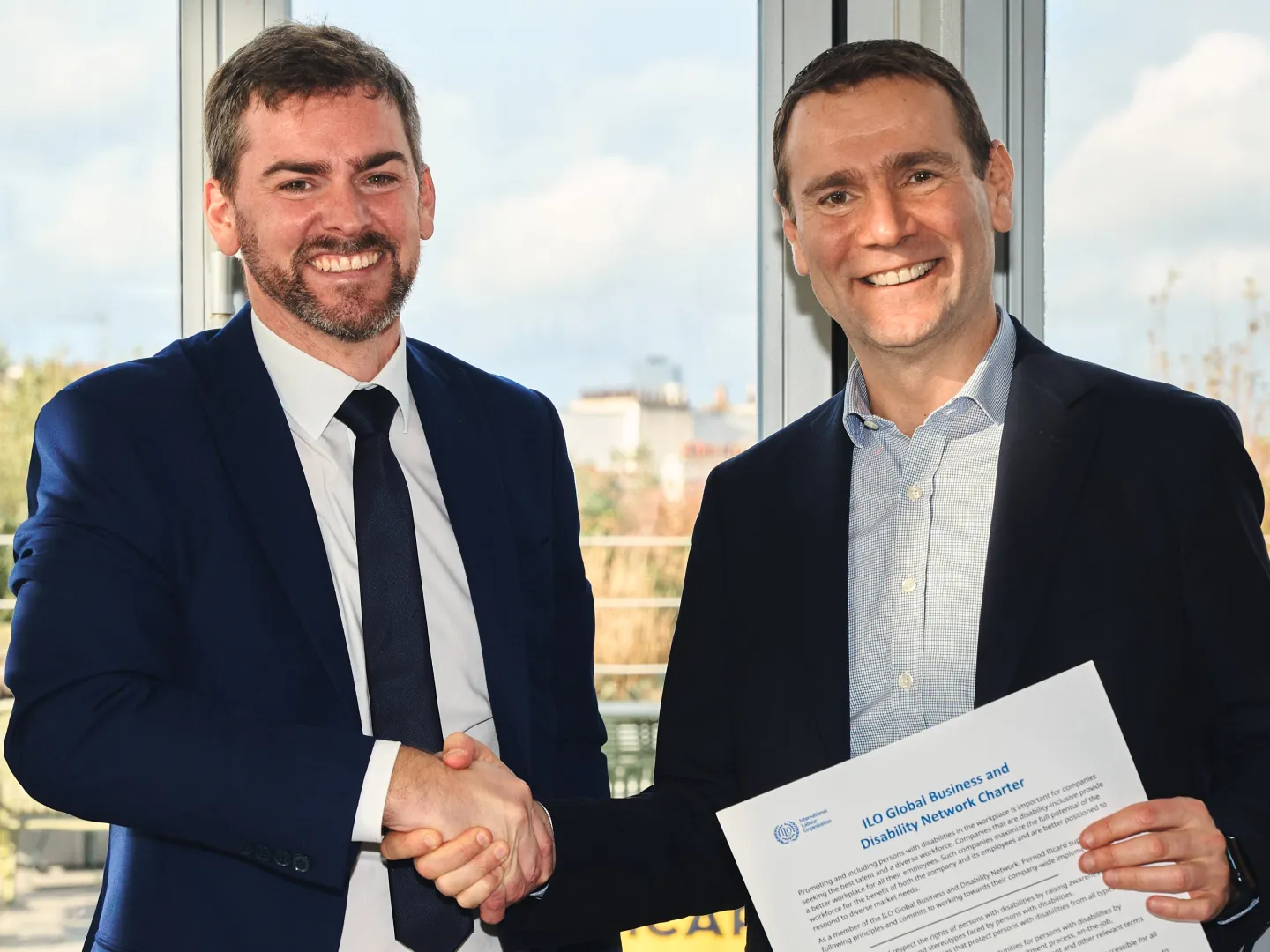 Jürgen Menze, Disability Inclusion Specialist at the ILO shaking hands with and Alexandre Ricard, CEO of Pernod Ricard while Alexandre is holding the GBDN Charter.