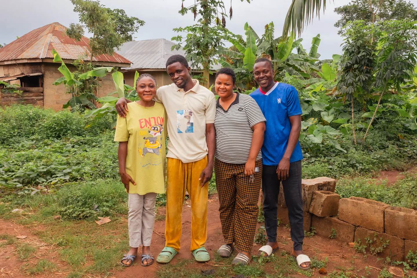 Oyefunde Bukola stands with three other young community members and ACCEL Africa beneficiaries in Aponmu, Ondo State. The group smiles warmly at the camera, surrounded by green vegetation and their houses in the background.