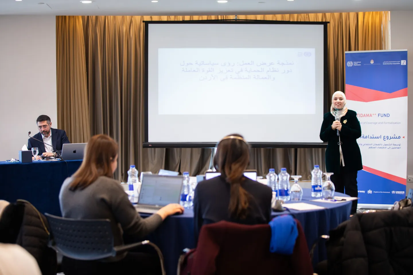 Rana Al-Ansari, ILO Officer, with microphone at a meeting