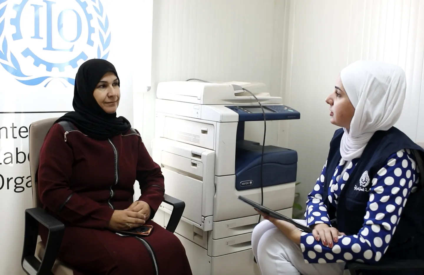 Tailor Malika Abdel-Rahim Al-Haraki speaks with ILO data collection officer Esra Bany Ersheed in the ILO-run Zaatari Office for Employment (ZOE) in Jordan’s Za’atari camp for Syrian refugees on October 28, 2025. 