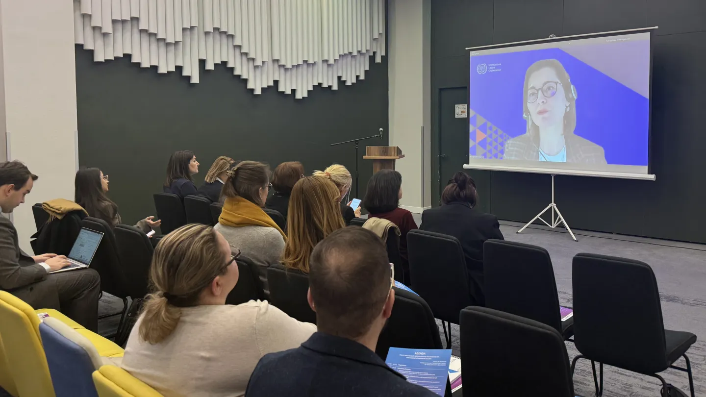Participants seated in a conference room watch a presentation on a screen