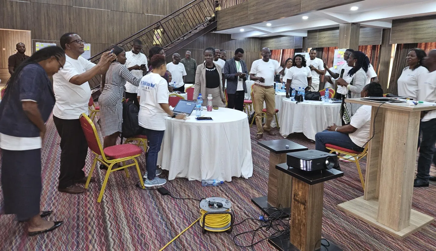 Participants in a training hall gathered around tables, interacting during an ILO cooperative development training session with laptops, materials, and presentation equipment visible.
