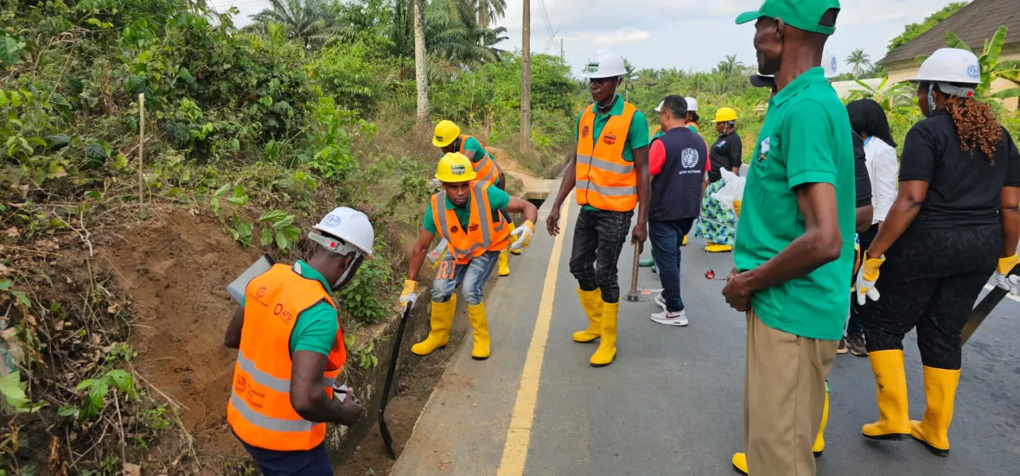 Workers wearing hard hats, reflective vests, and yellow boots clear a roadside drainage channel during a hands-on field training activity.
