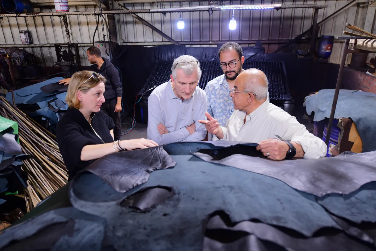 Four individuals are standing around a pile of leather pieces as they have a conversation.