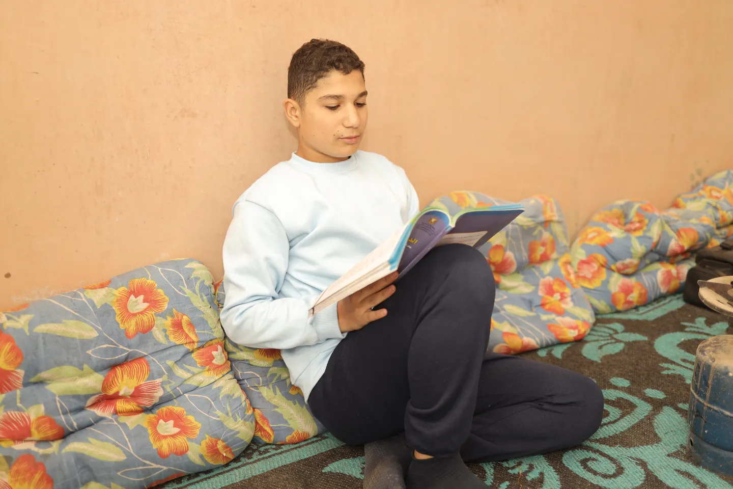 A young boy is seated on cushions looking at a book in his hand.