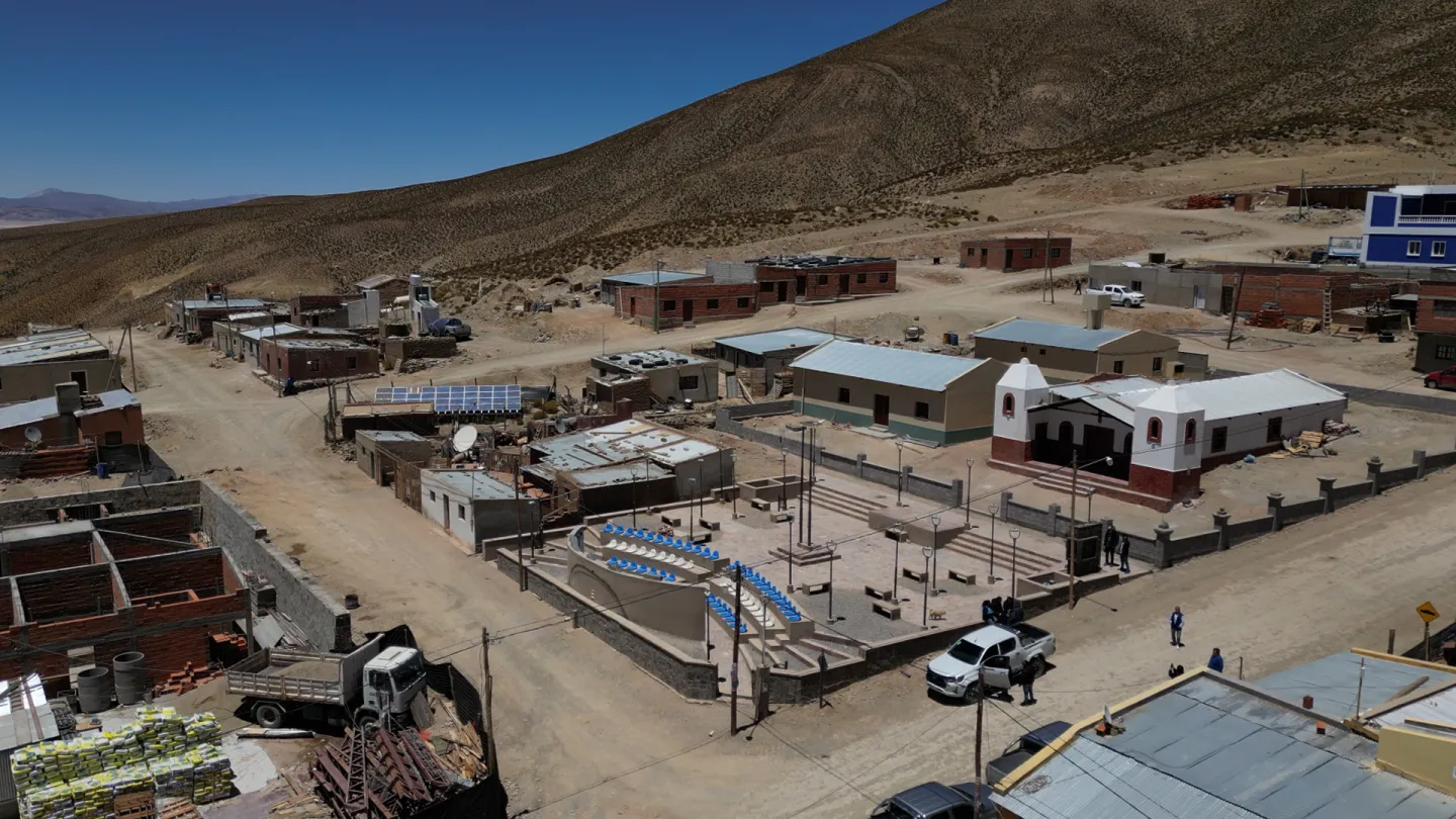Vista aérea de un pequeño pueblo en la Puna jujeña, Olaroz Chico,, con viviendas bajas de ladrillo, una plaza con anfiteatro y una iglesia, rodeado de paisaje árido y montañoso