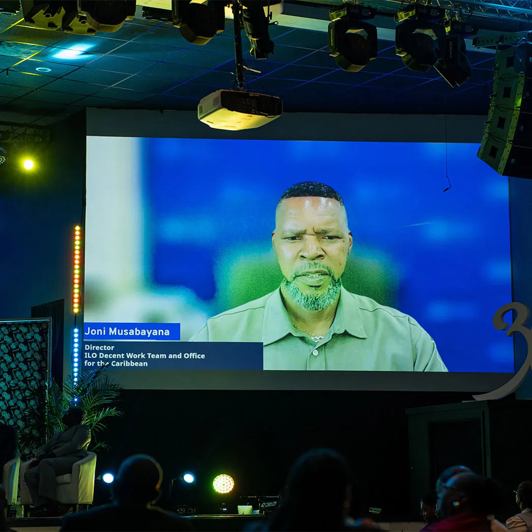 A wide photograph captures a large, projection screen projecting the video message by Joni Musabayana, Director, ILO Caribbean Office at the Annual General Assembly, National Tripartite Council (NTC) The Bahamas on 26 March 2026.