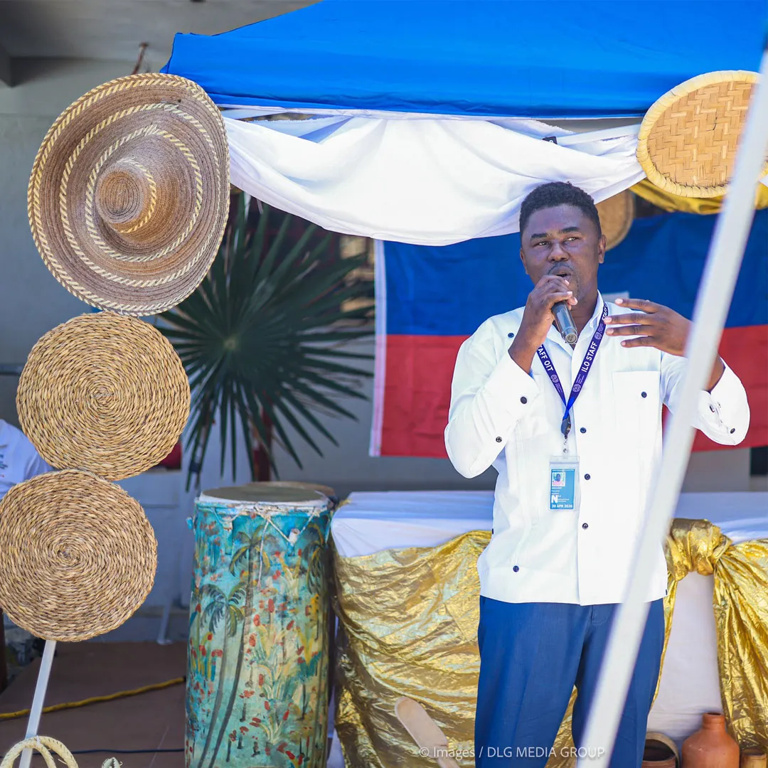 A man of African descent wearing a crisp white long-sleeved guayabera-style shirt and blue trousers. He wears a blue "ILO STAFF" lanyard with an official identification badge.
