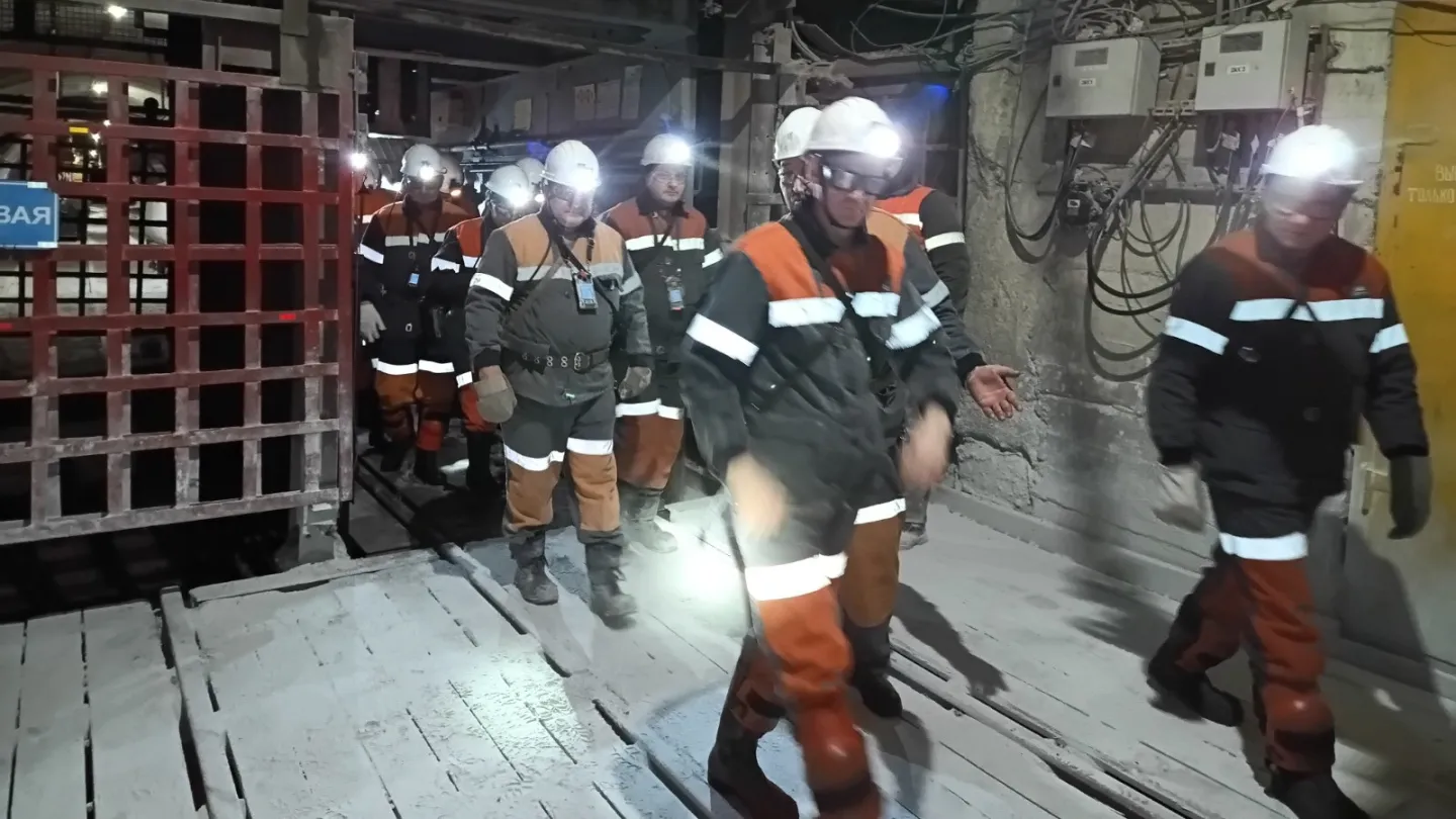 Group of people in protective gear stepping out of a mine elevator underground 