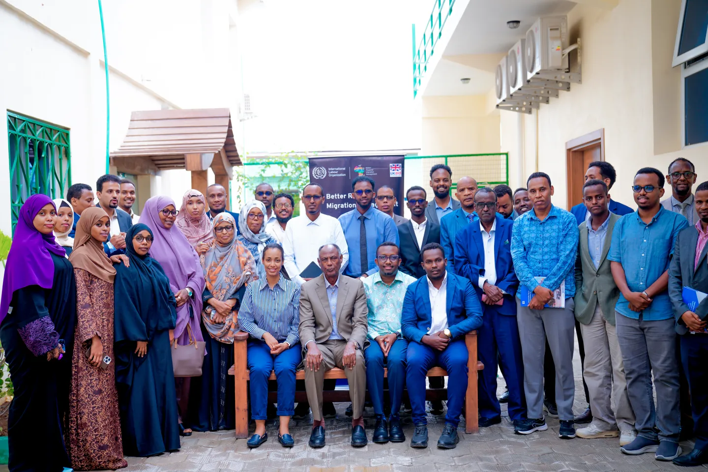Group photo of workshop participants standing and seated outdoors in front of an ILO BRMM banner during a labour migration policy event in Mogadishu, Somalia.
