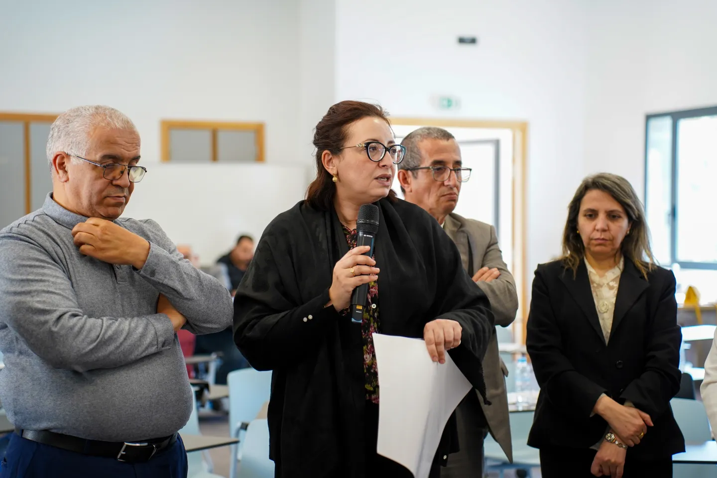 Une participante prend la parole avec un microphone lors d’un atelier, devant un groupe de participants assis autour de tables.