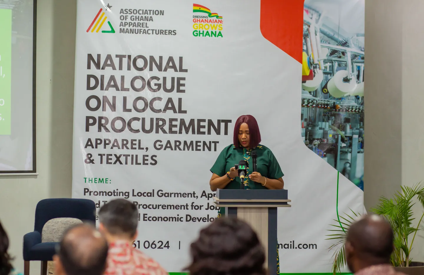 A woman speaks at a podium during a conference on local procurement for Ghana’s apparel, garment, and textile industry, with a large event banner behind her