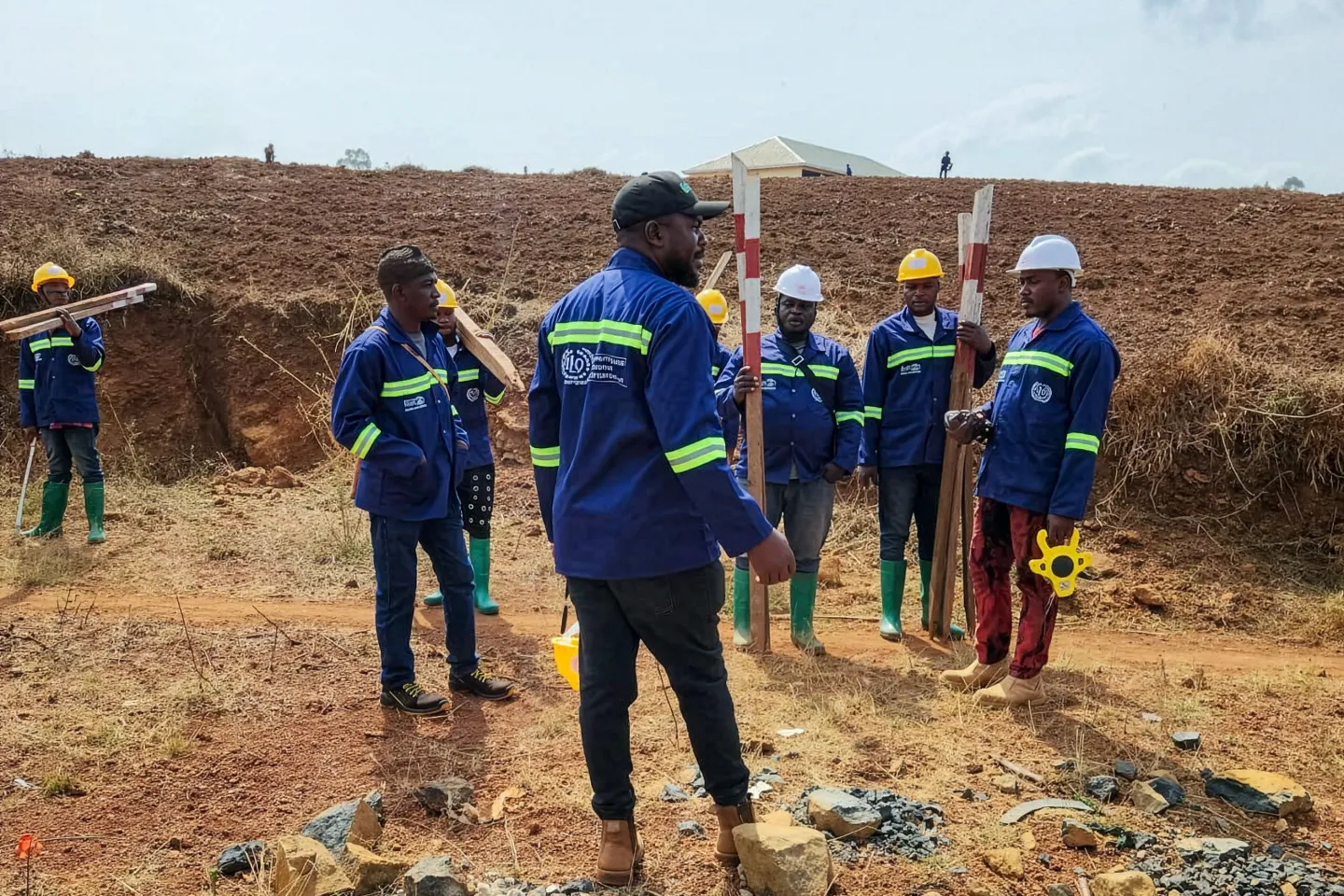 Engineers inspect a road rehabilitation site in Nkambe with workers in safety gear.