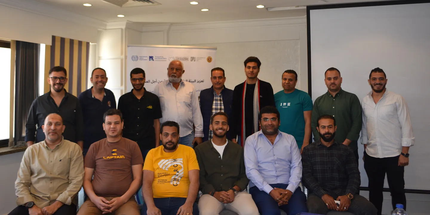 Group photo of trainees seated in the front row and standing in the second row, in front of a presentation wall and project rollup banner.