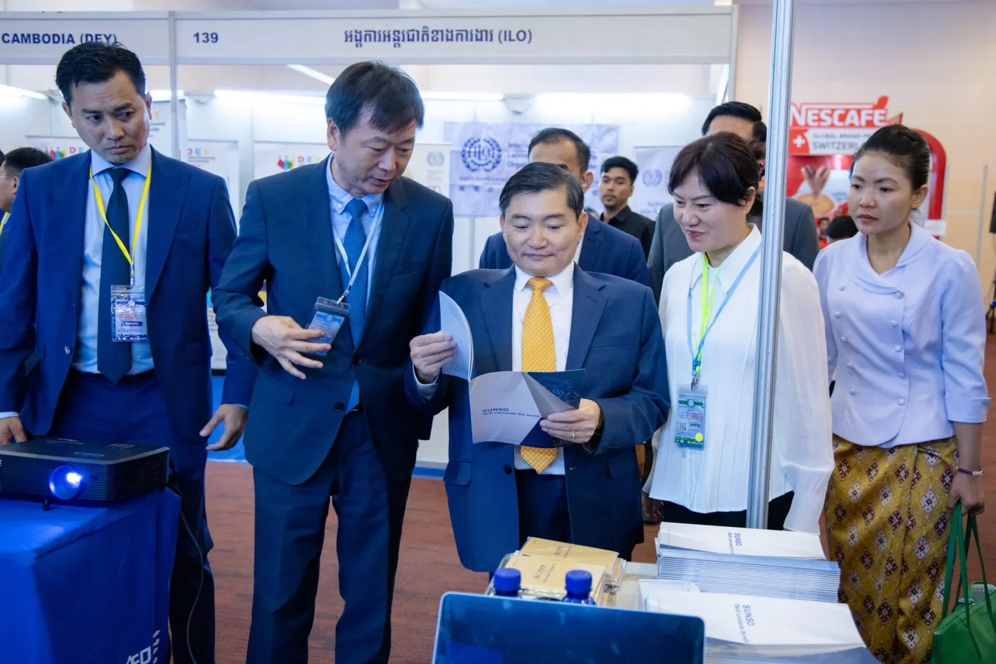 Standing around a display table, several officials and participants look at a publication.