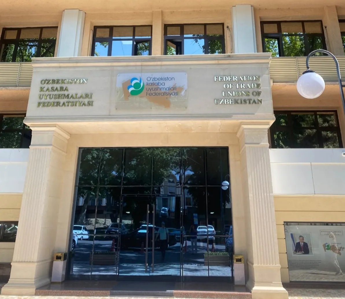 Photograph of a building entrance with signage for the Federation of Trade Unions of Uzbekistan in both Uzbek and English. 