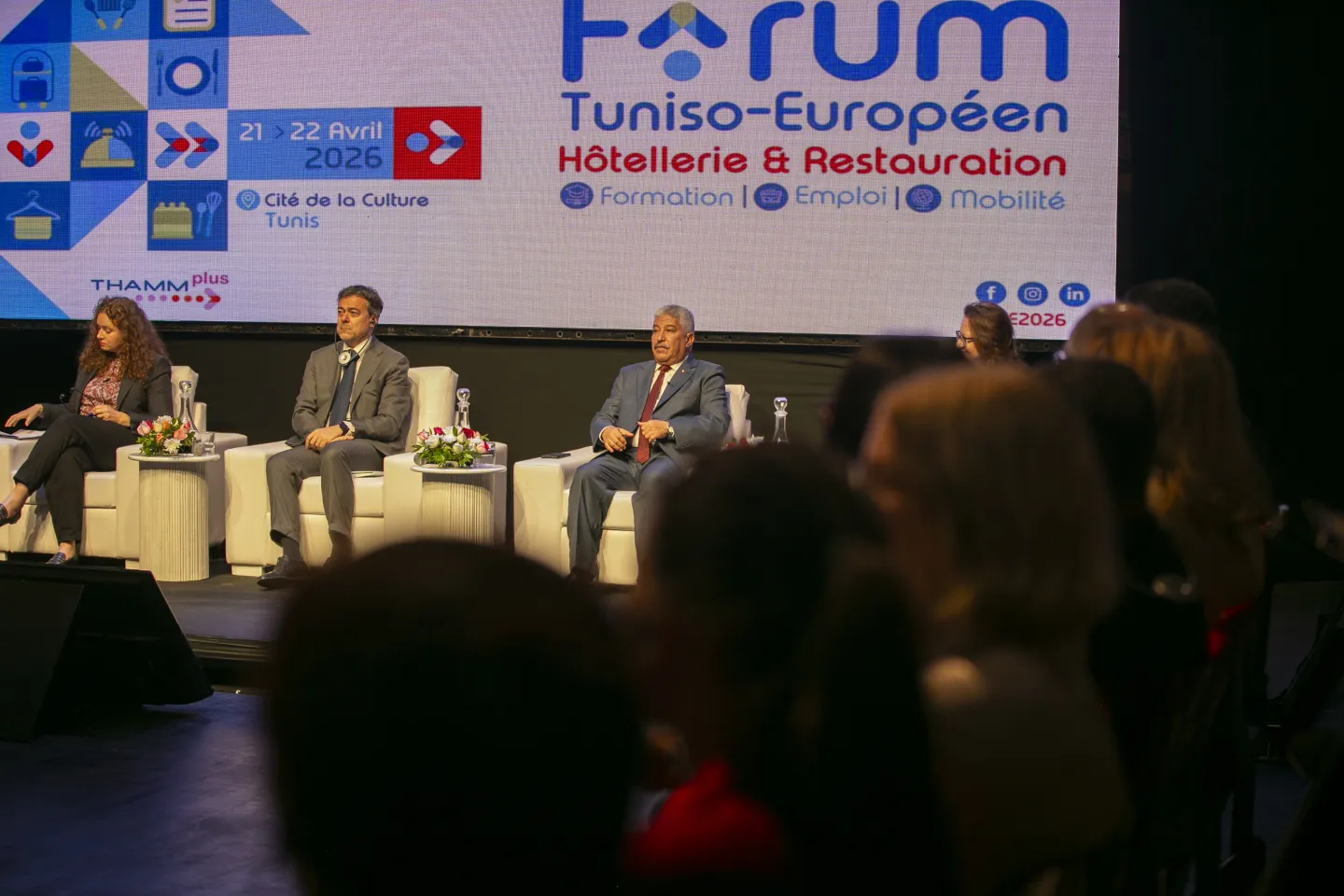 M. Riadh Chaoued, ministre de l’Emploi et de la Formation professionnelle, et M. Gianfranco Bochicchio, Chef adjoint de la Délégation de l’Union européenne en Tunisie, sont assis sur scène lors d’un panel du Forum tuniso-européen de l’Hôtellerie & de la Restauration. En arrière-plan, un grand écran affiche le visuel de l’événement
