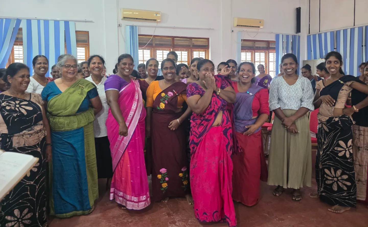A group of women stand together in a classroom, smiling and laughing.