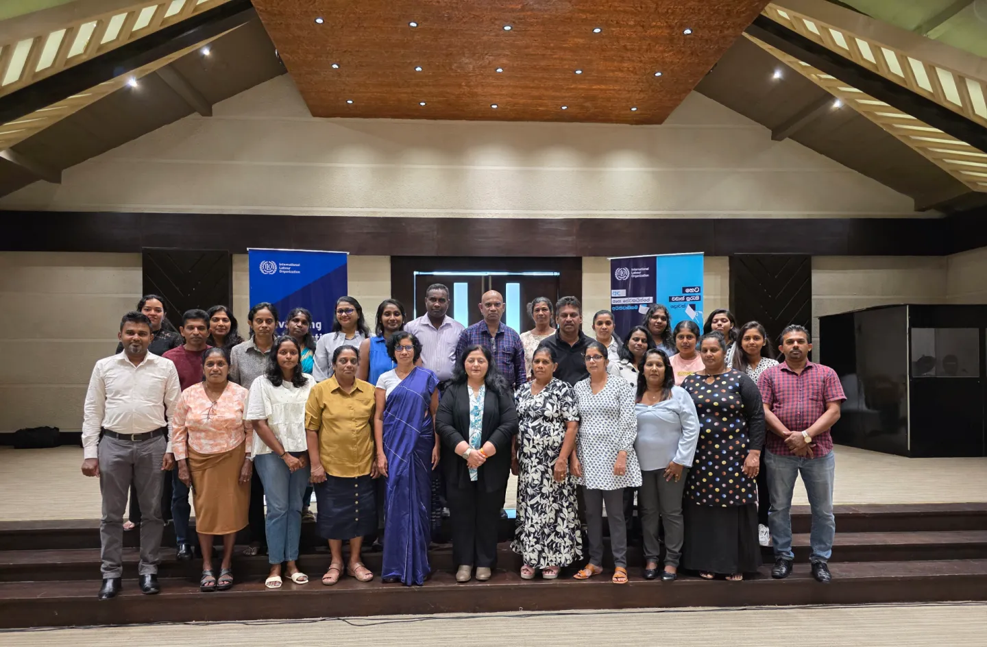A group of participants pose for a photo on a stage.