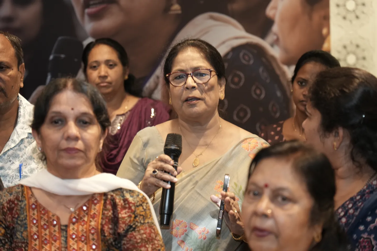 A woman speaks into a microphone while other participants listen around her.