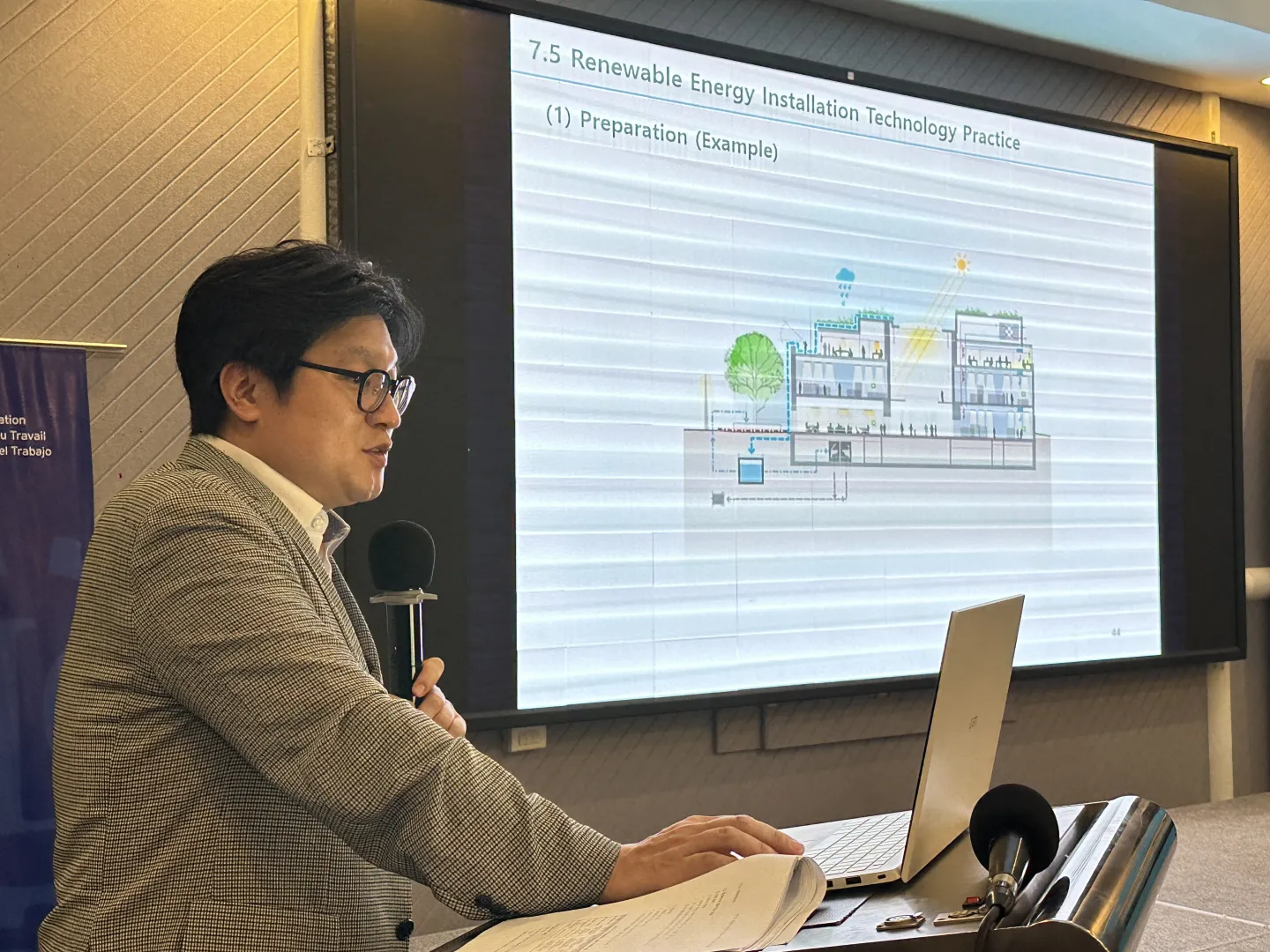Training instructor while renewable energy installation is shown on screen.