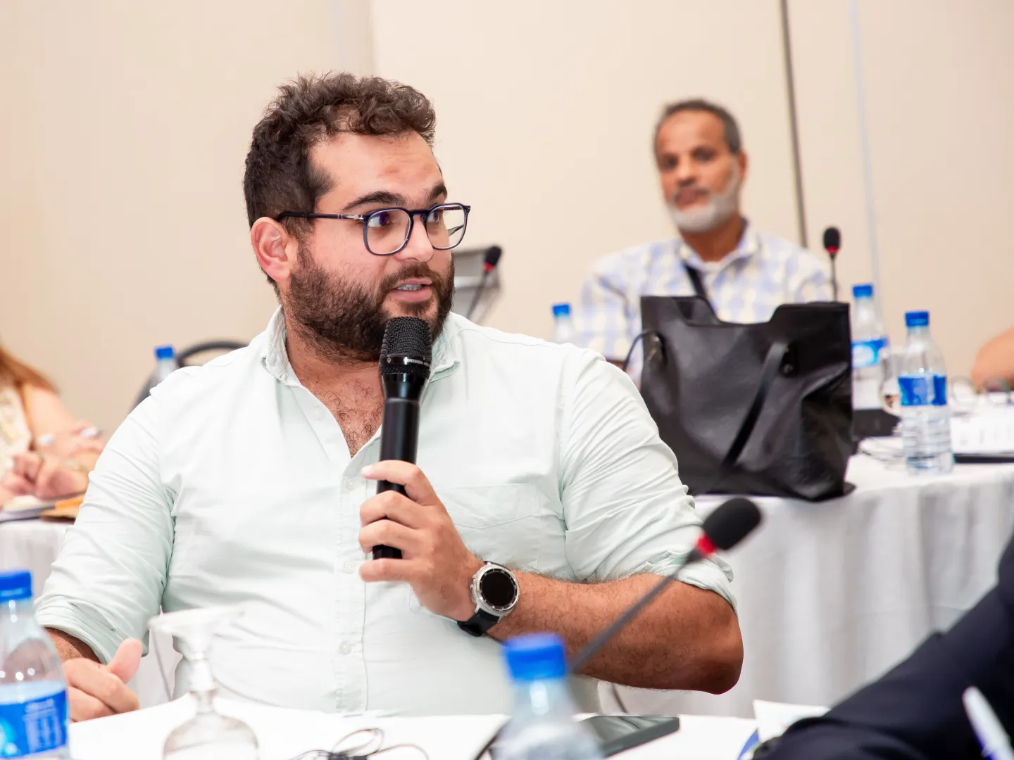 Un participant s’exprime avec un microphone lors d’une séance de travail organisée dans le cadre du lancement de la deuxième phase du programme METI en Tunisie. D’autres participants suivent les échanges autour de la table.