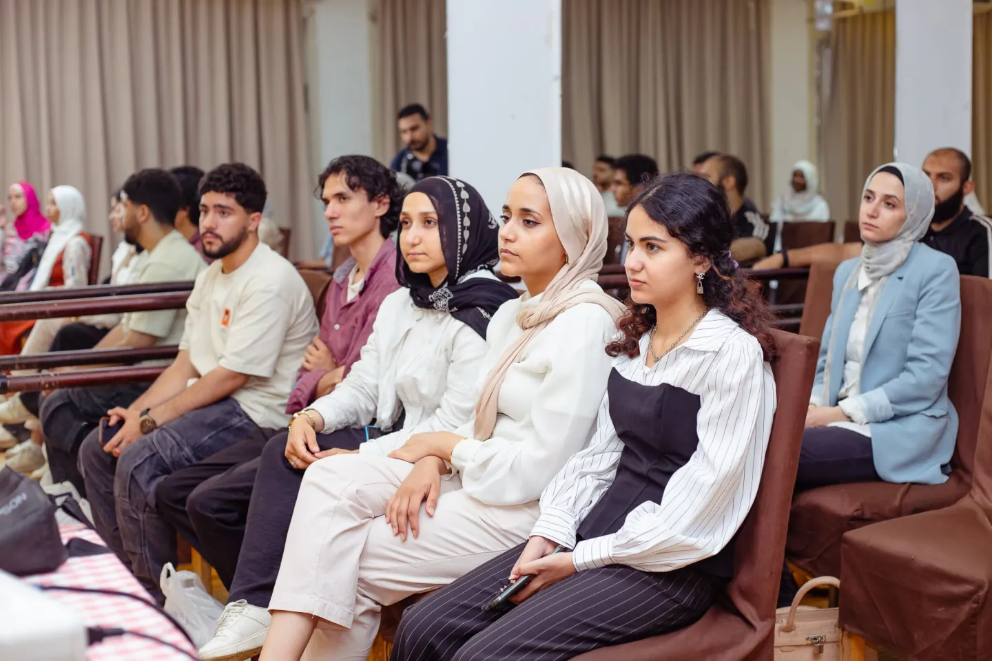 Young men and women are seated indoors, attentively participating in a workshop.