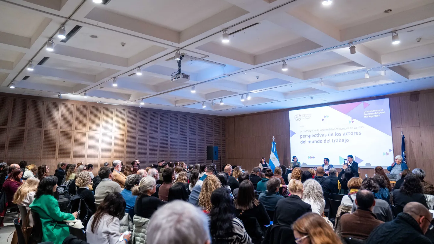Alt text: Panel “La transición hacia la formalidad en tiempos de cambio: perspectivas de los actores del mundo del trabajo” durante el IX Seminario sobre Economía Informal de la OIT en Argentina. Panelistas conversan en el escenario frente a un auditorio con amplia participación de público.
