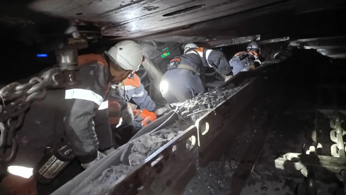 Mineros agachados en un espacio reducido dentro de un túnel de mina. La única luz procede de sus lámparas frontales.