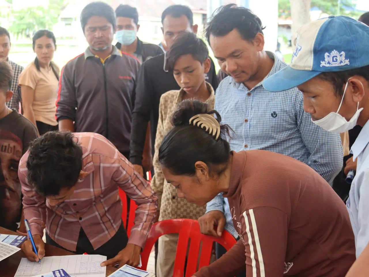 People completing documents while others stand and observe. 