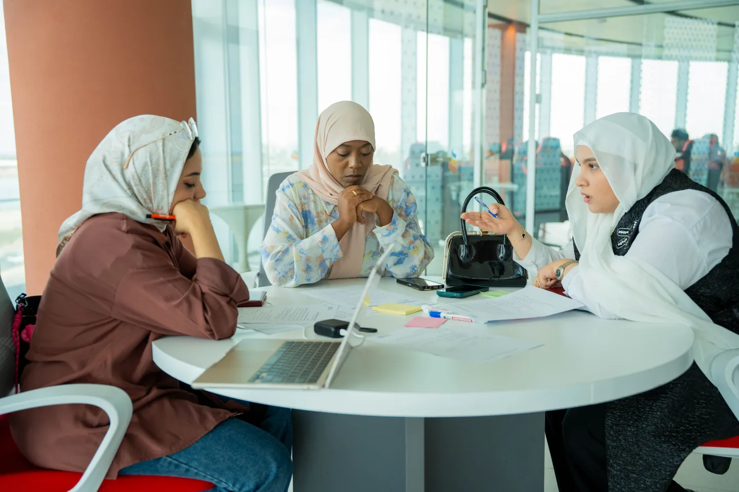 Three women discuss workshop materials around a table during a group session