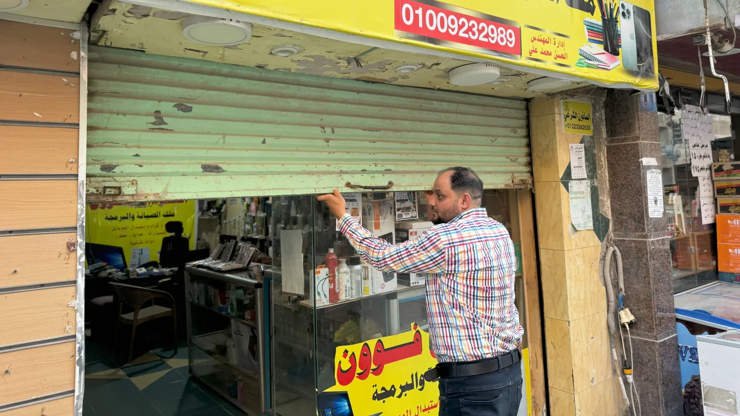 Alhassan Ali raises the storefront shutter of his mobile phone repair shop.