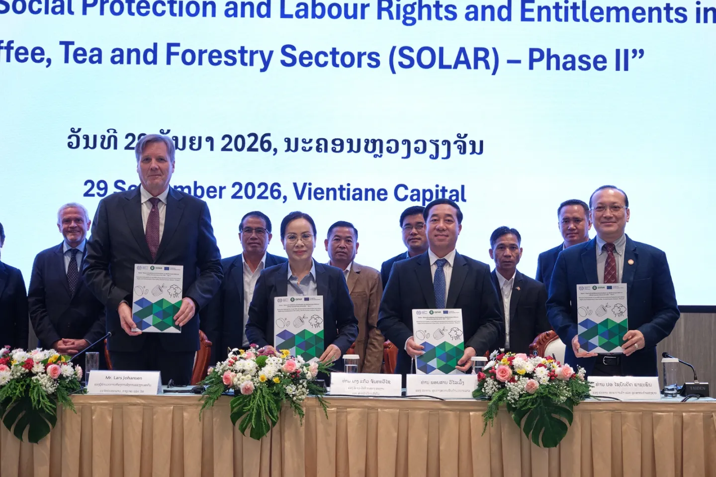 People stand on a stage and pose with project documents. 