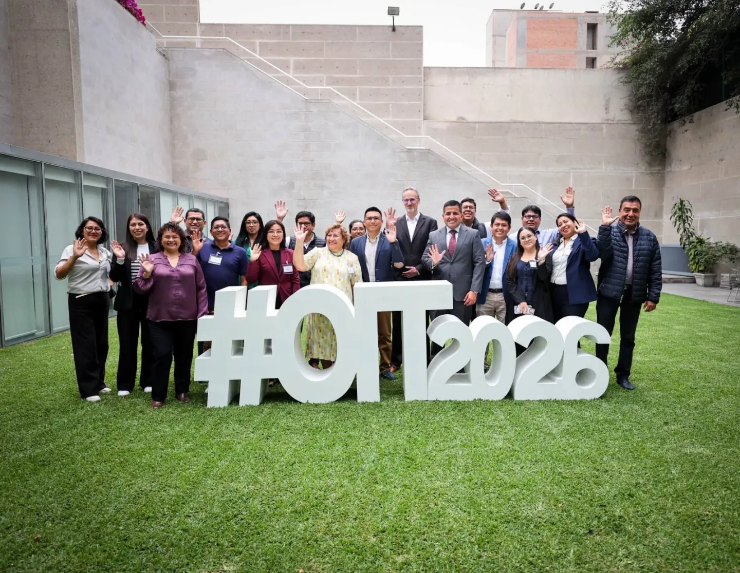 Grupo de personas posando frente a cámara, saludando con la mano, en un jardín