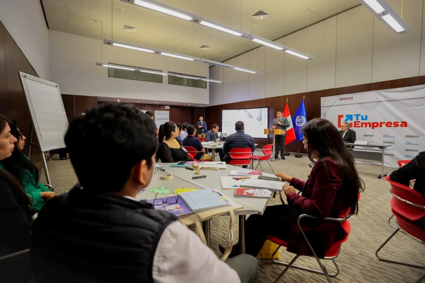 Participantes escuchan una exposición durante taller sobre salarios digitales, con las banderas del Perú y la OIT al fondo visibles.