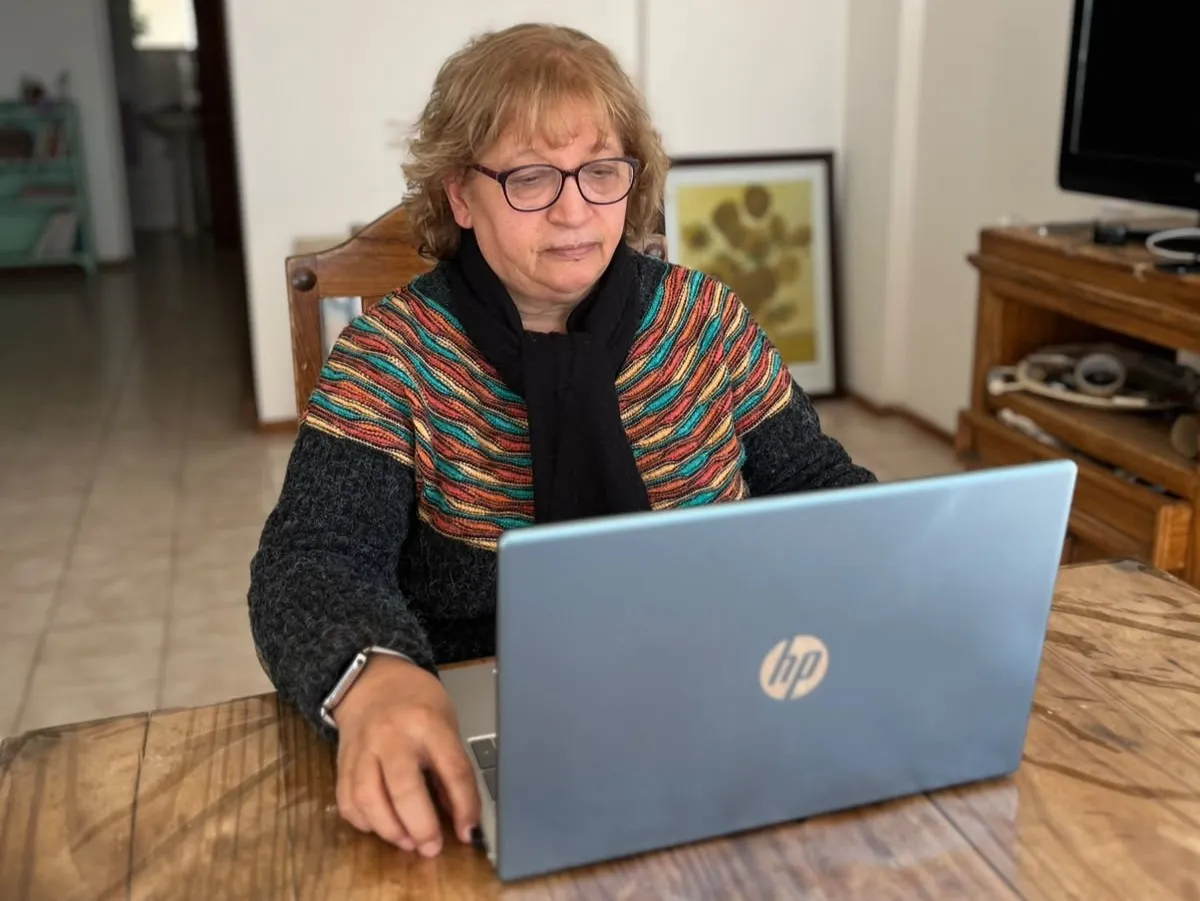 Mujer utiliza una computadora portátil mientras trabaja desde la mesa de su hogar.
