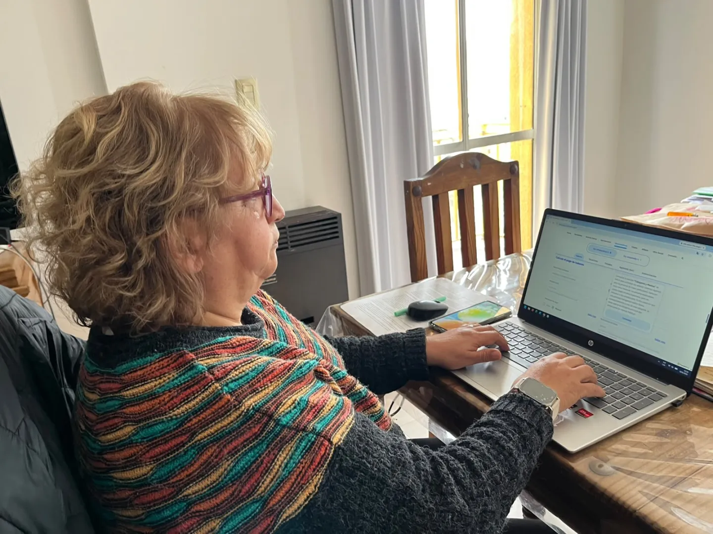 Mujer utiliza una computadora portátil mientras trabaja desde la mesa de su hogar.