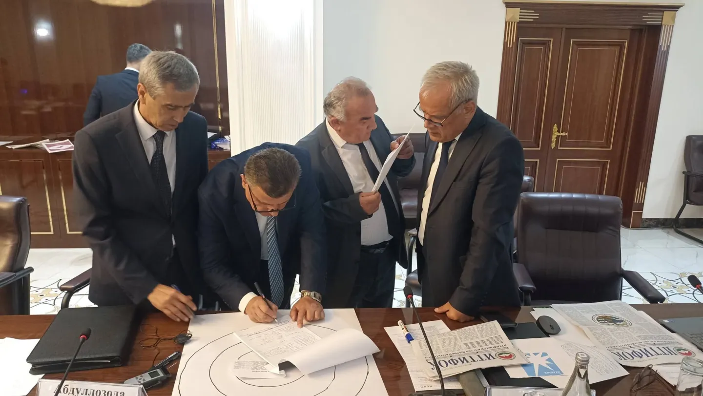 Four men work together over papers and a diagram on a conference table