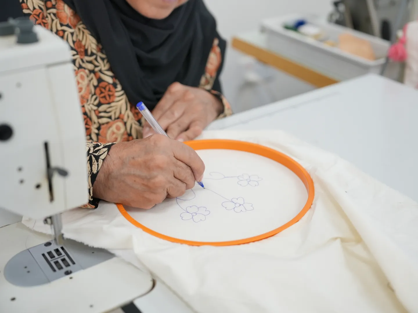A woman draws a floral pattern on fabric beside a sewing machine in Petra, Jordan.