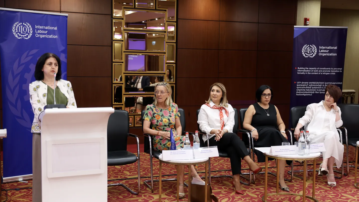 A woman speaking at a podium and four panellists seated beside her