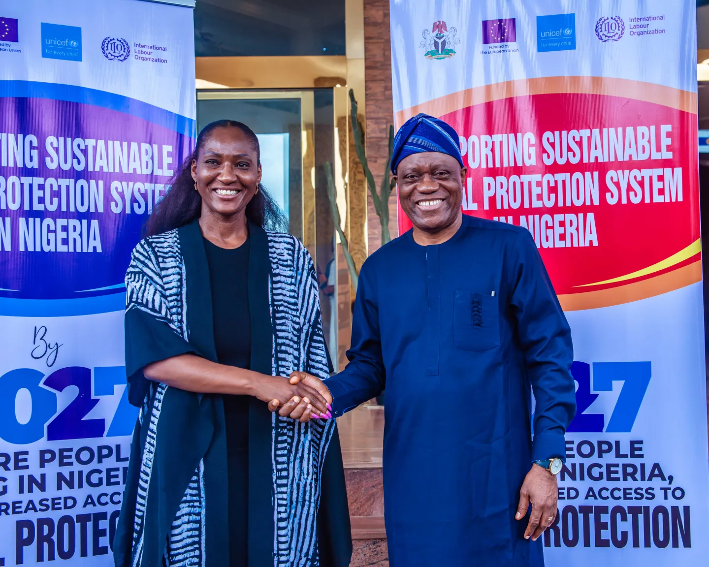 Dr Vanessa Phala and Prince Adeyemi Adeniran smile and shake hands between banners promoting a sustainable social protection system in Nigeria.