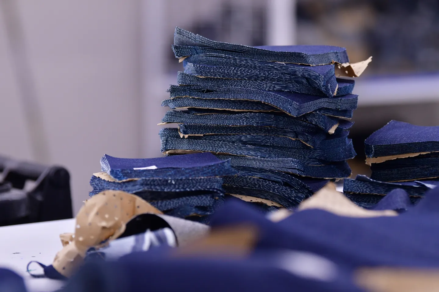 Pieces of denim fabric cut into square shapes are stacked on a table.