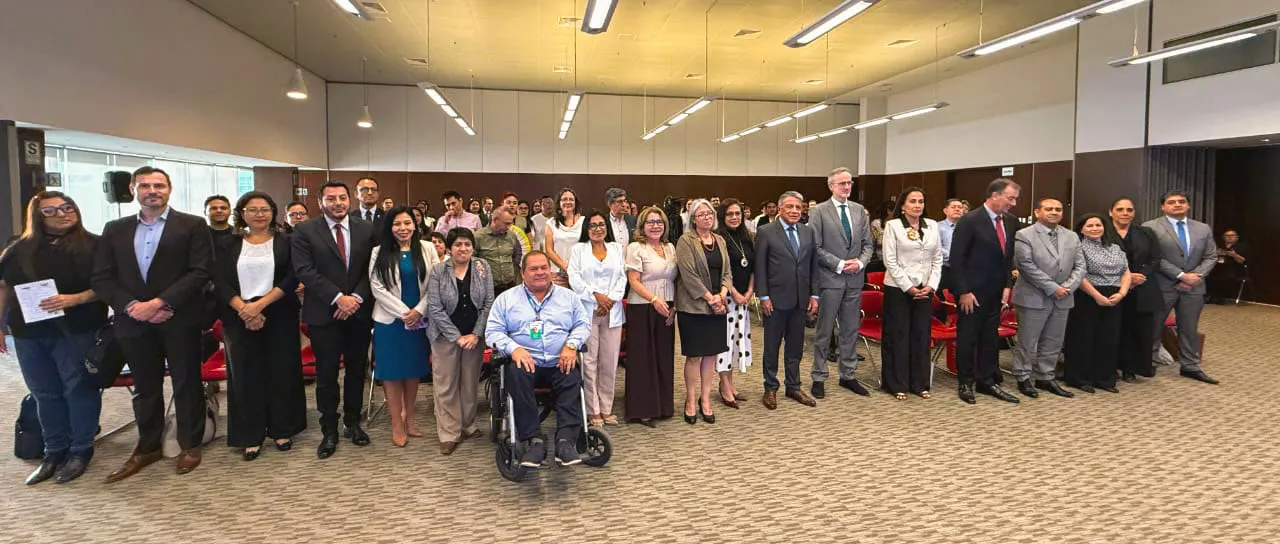 Grupo numeroso de personas de pie y sentadas posa para una fotografía dentro de un auditorio.