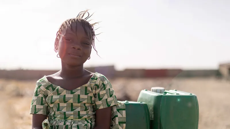 A young girl dressed in green sitting next to two green bottles of water